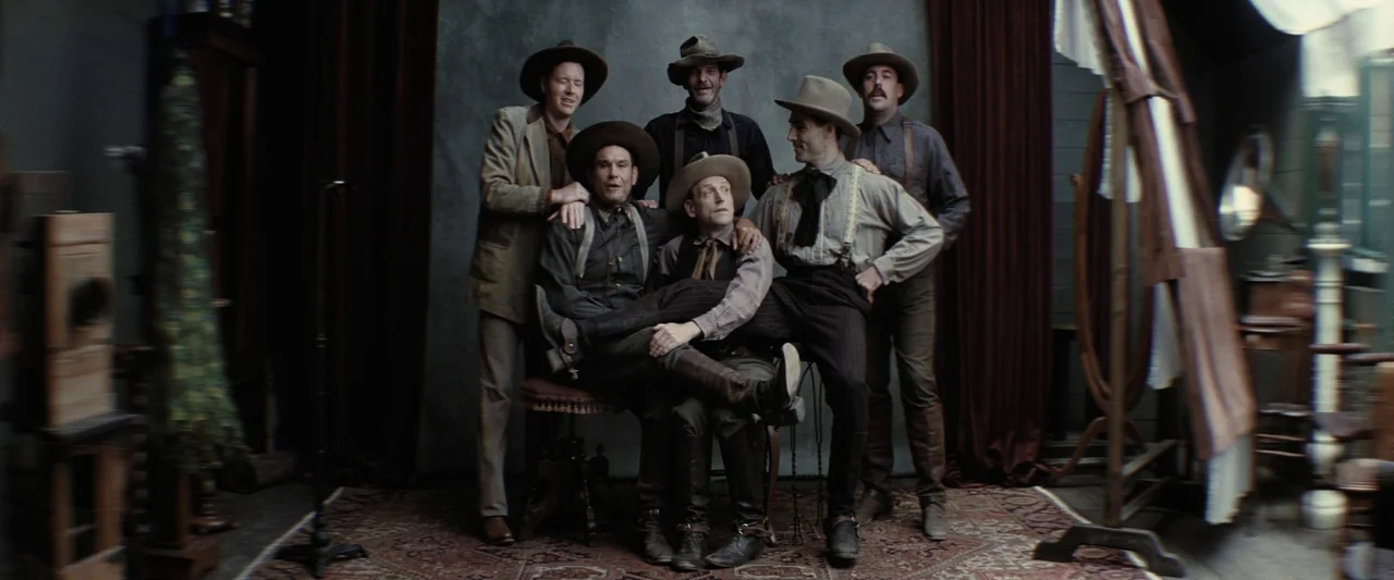 Killers of the Flower Moon (2023) movie still: fullbody — An 1880s photography studio features a gray muslin backdrop and an ornate area rug. Six…