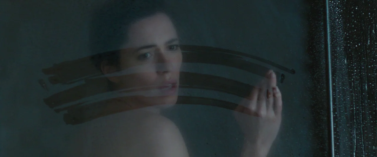 The Gift (2015) movie still: closeup — A dark, steamy bathroom shower features a glass partition covered in condensation. A woman presses her hand…