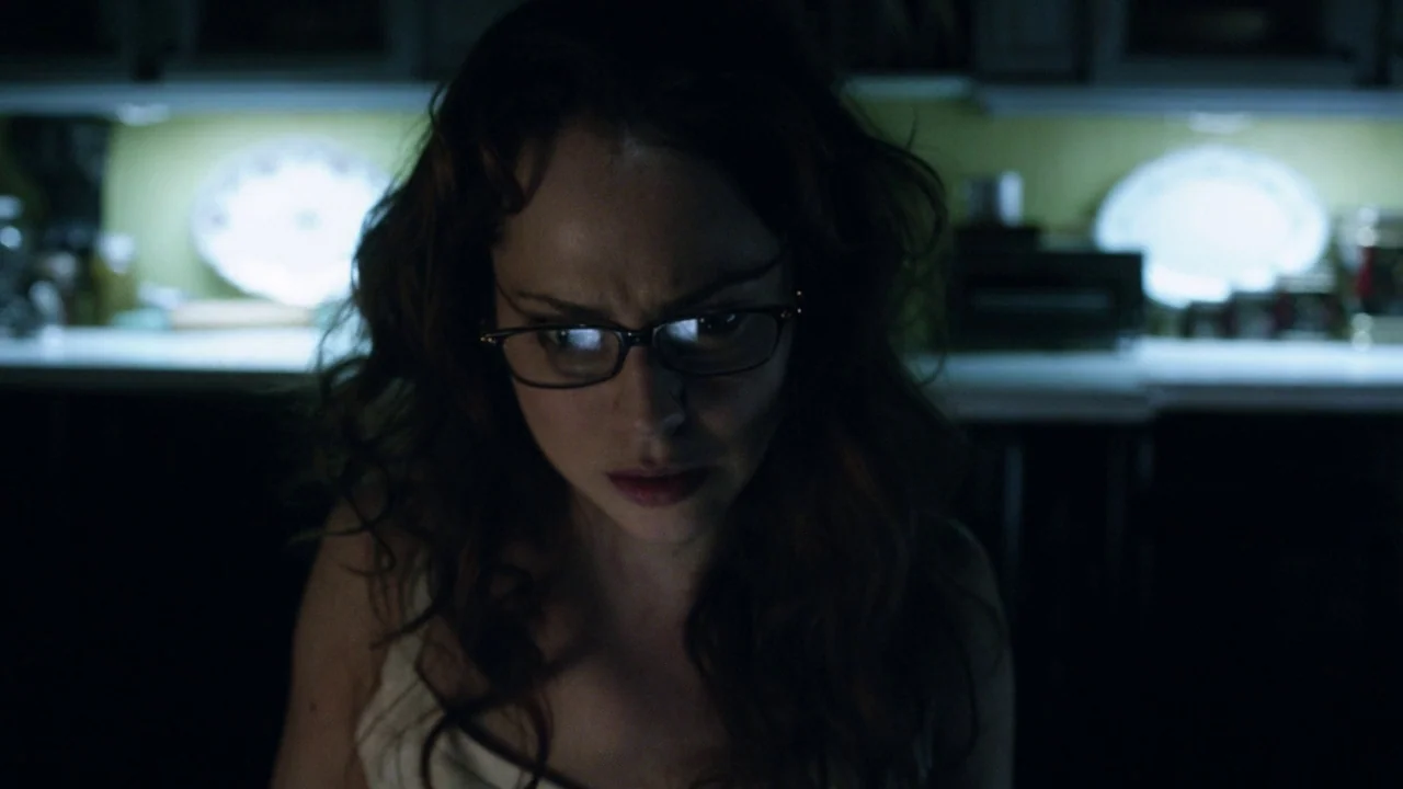 Curse of Chucky (2013) movie still: closeup — A dimly lit room features a woman illuminated by light from a digital screen. She looks downward with…