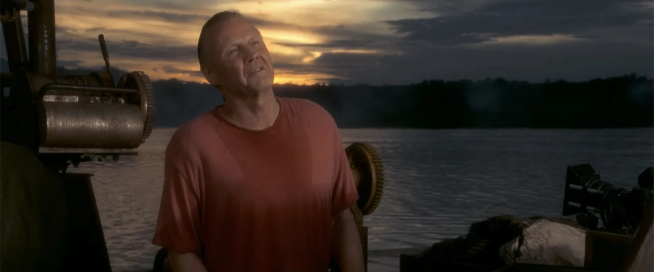 Anaconda (1997) movie still: medium — A man stands on the deck of a boat against a sunset backdrop. The subject faces away from the camera toward…