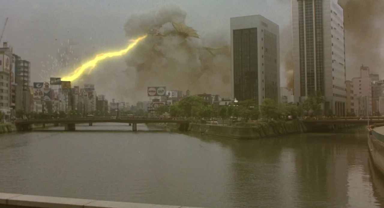 Godzilla vs. King Ghidorah (1991) movie still: wide — A wide view of a river crossing a Japanese city with multiple office buildings. A large flying…