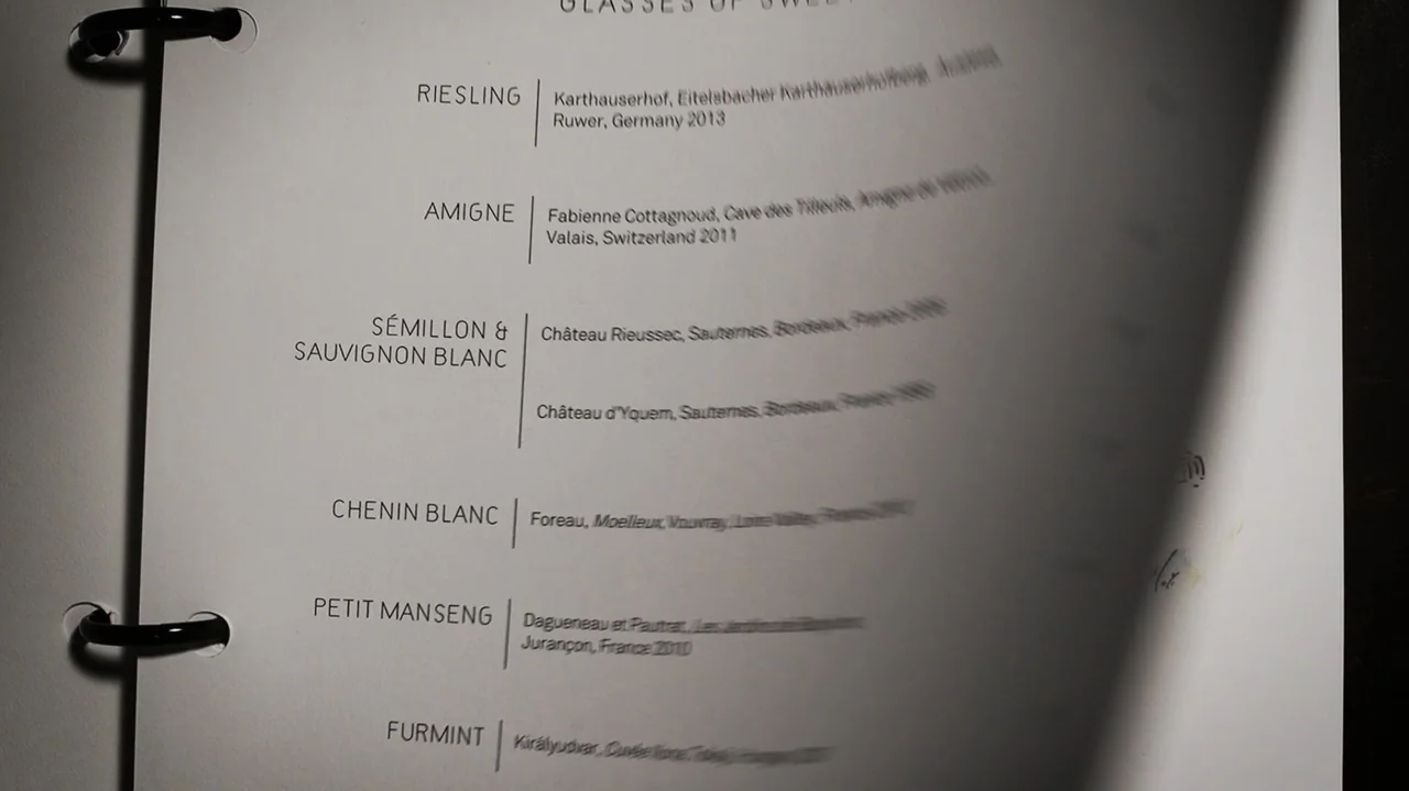 Somm: Into the Bottle (2015) movie still: closeup — A close up view of a white paper wine menu held in a binder. The right edge of the page is…