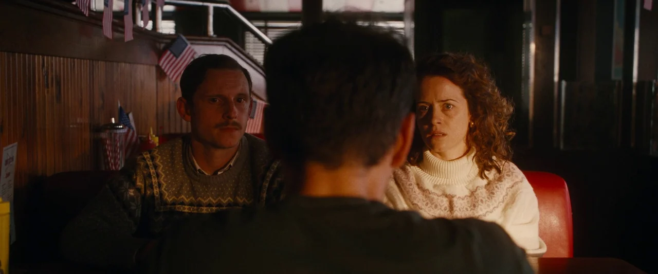 All Of Us Strangers (2023) movie still: medium — A dark restaurant booth with wood-paneled walls decorated with small American flags. A man and a…