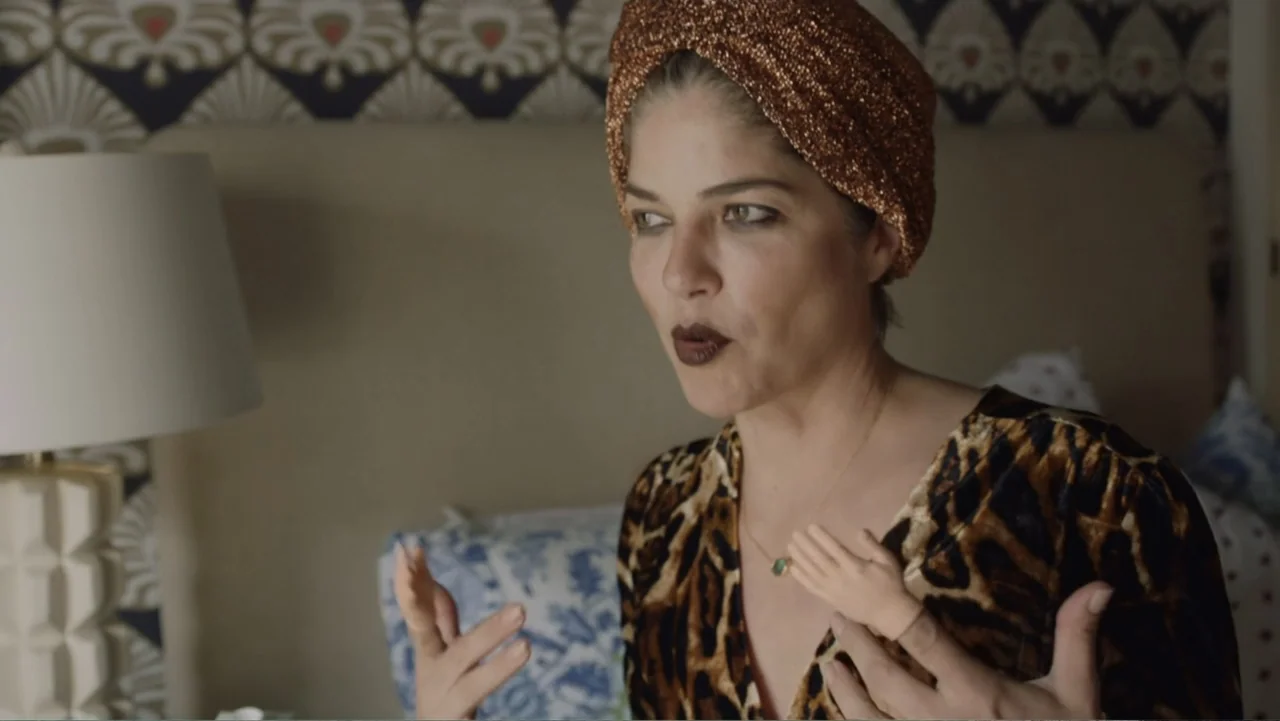 Introducing, Selma Blair (2021) movie still: medium — A well-lit room features a headboard with blue and white patterned wallpaper background. A…