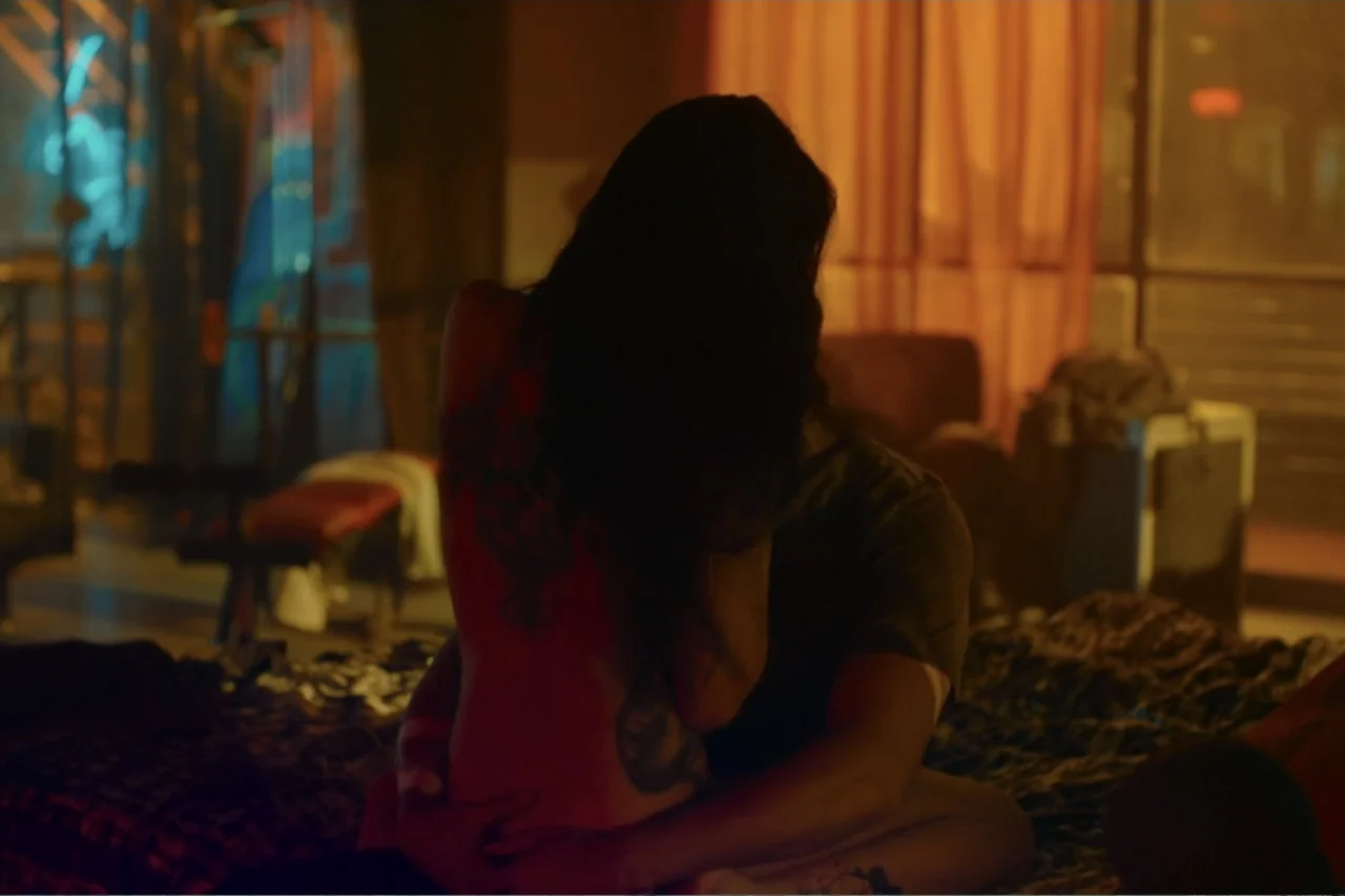 Cross the Line (2020) movie still: medium — A dimly lit room features a patterned bed spread and orange curtains in the background. A woman seen…