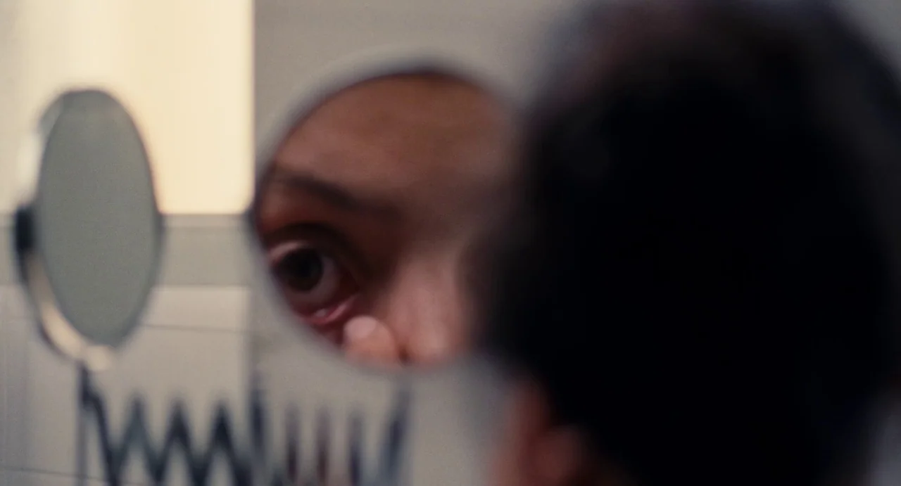 Ava (2017) movie still: closeup — A close-up view of a human eye reflected in a small circular vanity mirror. The person is adjusting their eyelid…