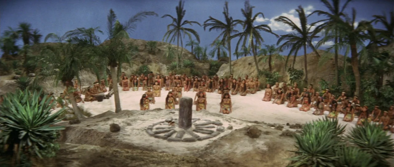 Ebirah Horror of the Deep (1966) movie still: wide — A clearing with sandy ground features a central stone pillar surrounded by small rocks. Many…