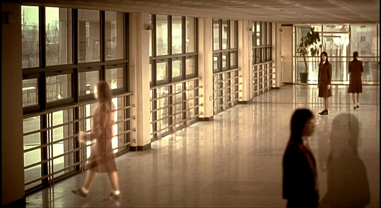 Voice (2005) movie still: wide — A long school corridor features polished floors and extensive glass windows along one side. Several students in…