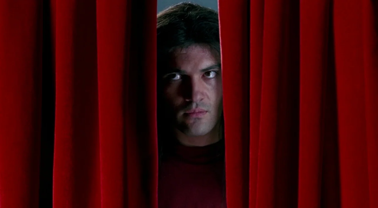 Tie Me Up! Tie Me Down! (1989) movie still: closeup — A man peers through a narrow opening between two thick, red velvet curtains. His face is…