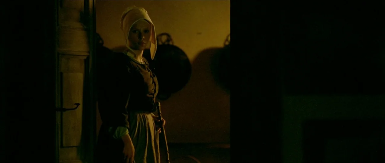 Girl with a Pearl Earring (2003) movie still: medium — A dark, sparsely furnished interior with shadows cast by large circular pans on walls. A…