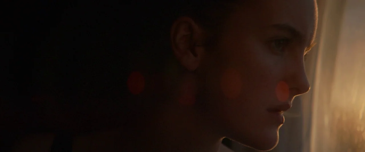 Kissing Candice (2017) movie still: closeup — A close up portrait of a young woman in a dimly lit bedroom setting. She stands near a window with…