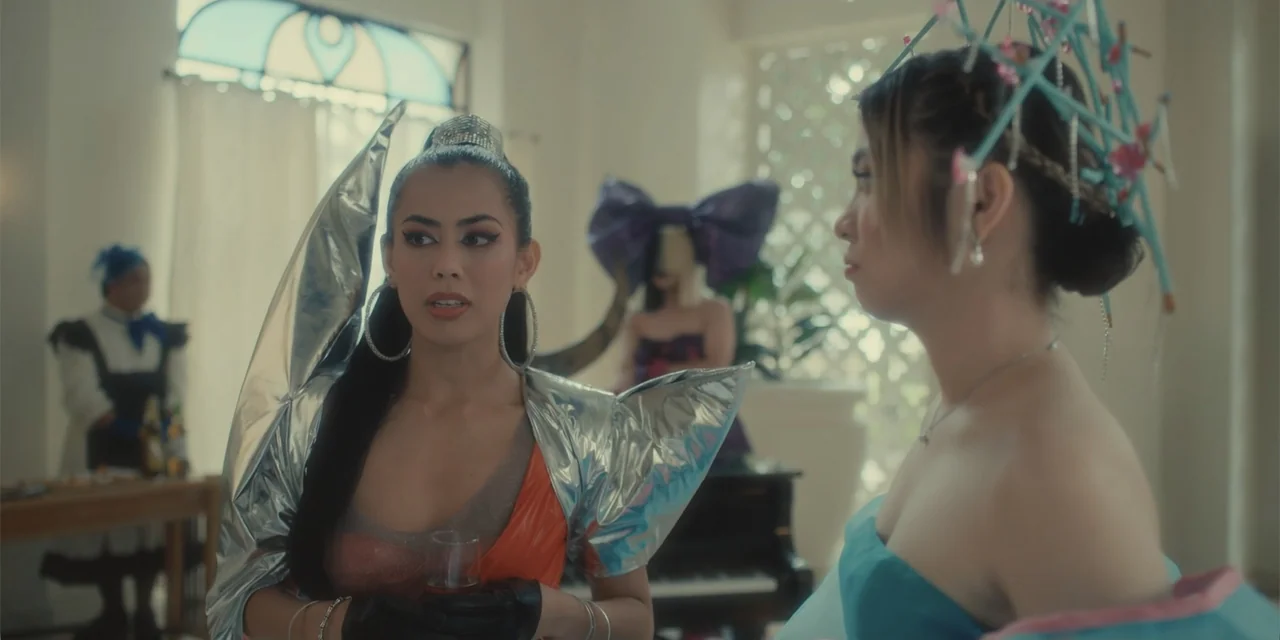 Ten Little Mistresses (2023) movie still: medium — An opulent interior space with large windows and a piano in the background. Two women wearing…