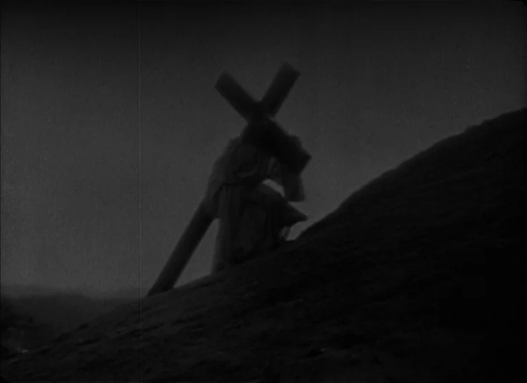The Kid (1921) movie still: fullbody — A dark, silhouetted figure climbs a steep, desolate hillside under a black sky. The individual carries a…