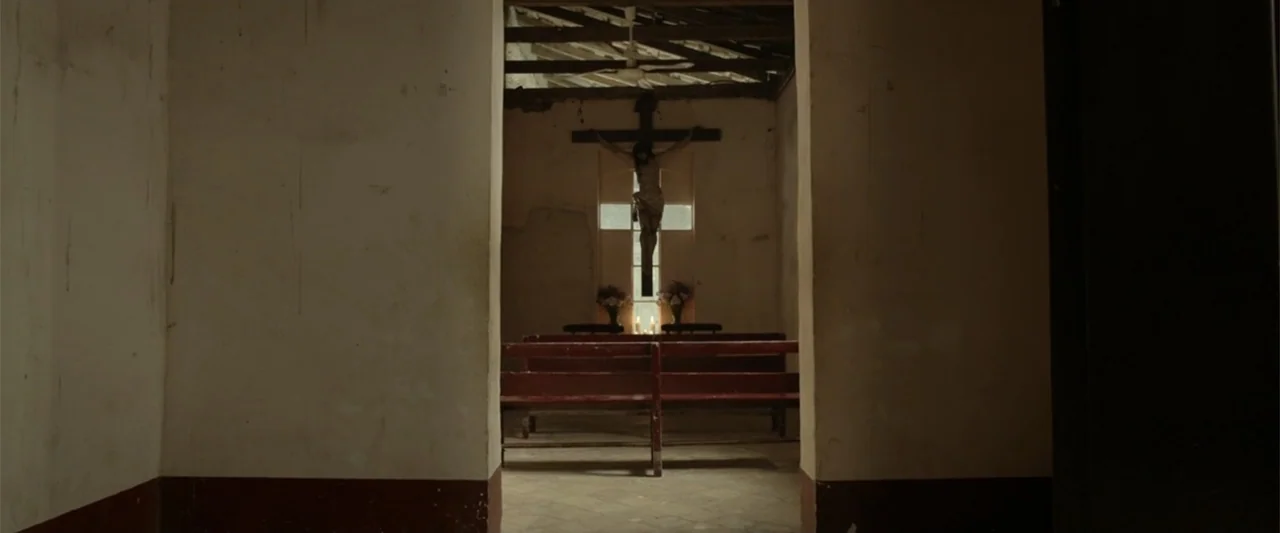 I Dream in Another Language (2017) movie still: medium — A small rustic chapel with red wooden benches stands viewed through a dark stone archway. A…
