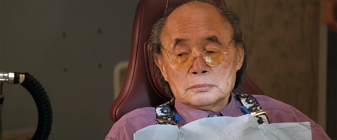 Lethal Weapon 4 (1998) movie still: closeup — An elderly man sits in a reclined professional chair within a sterile clinical space. He wears a…