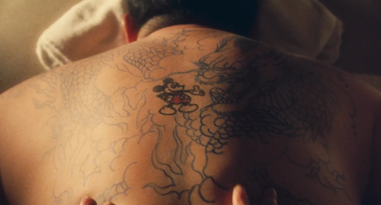 Comrades: Almost A Love Story (1996) movie still: closeup — A bare human back displays an intricate black ink dragon tattoo with a small Mickey…