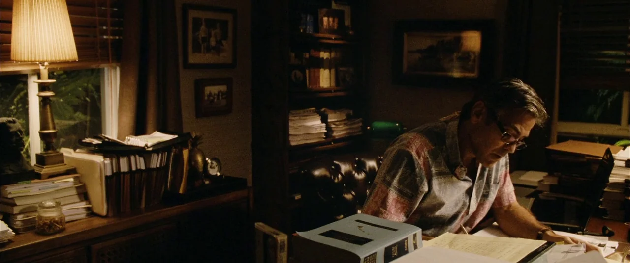 The Descendants (2011) movie still: medium — A cluttered personal study is filled with stacks of papers and professional files. A man sits at a…