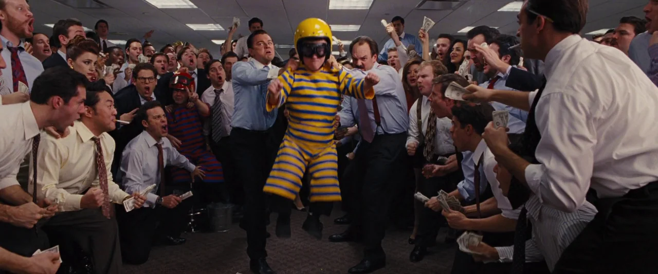 The Wolf of Wall Street (2013) movie still: fullbody — A crowded office space filled with men in shirts and ties cheering and waving money. A man in…
