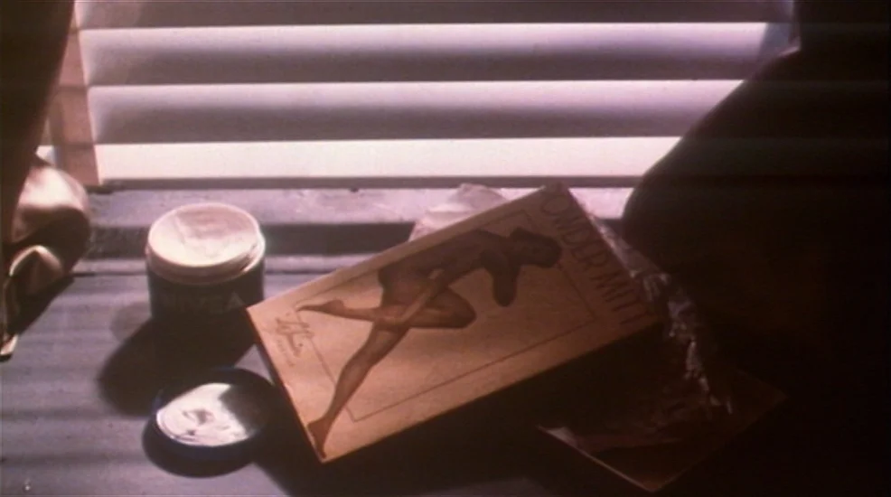 Union City (1980) movie still: closeup — A dark, flat surface holds a jar of Nivea cream and a Powder Mitt box. Horizontal slats of light cut across…