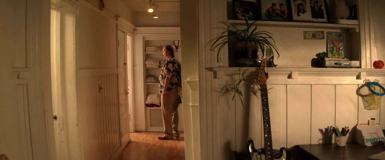 Seven Stages to Achieve Eternal Bliss (2018) movie still: medium — A residential hallway features white paneled walls and a built-in shelf unit with…