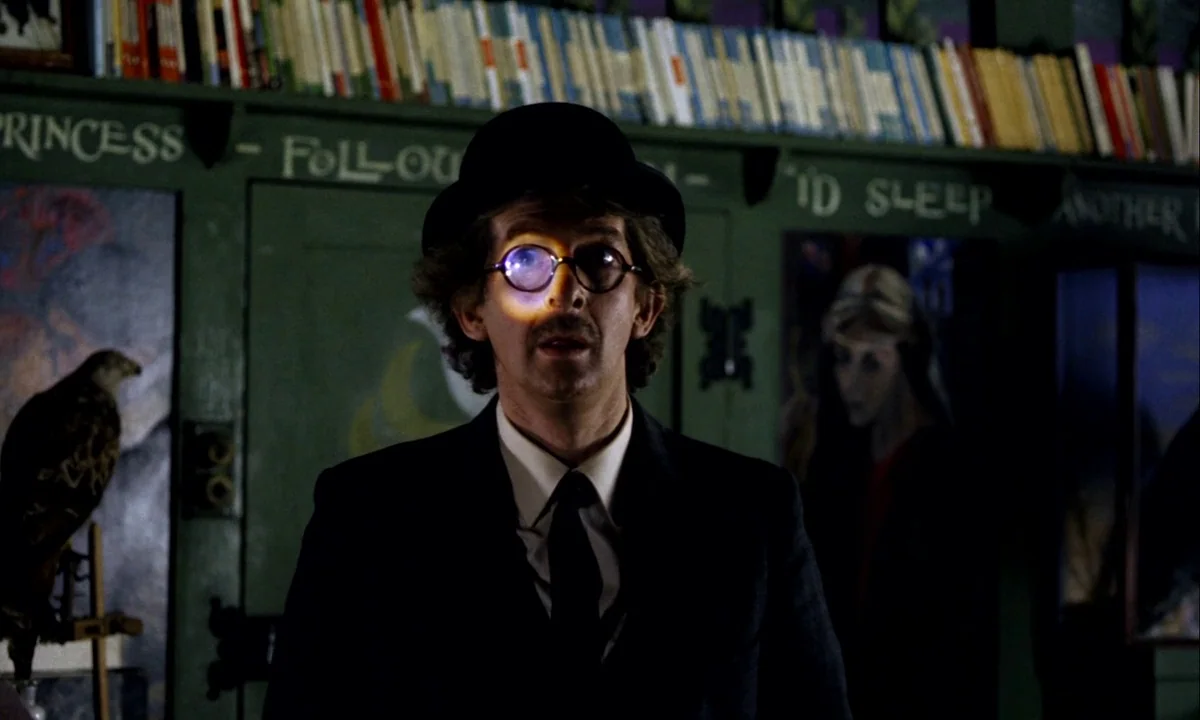 Wonderwall (1968) movie still: medium — A room with walls lined with books and hand-painted lettering on green panels. A man in a suit and bowler…