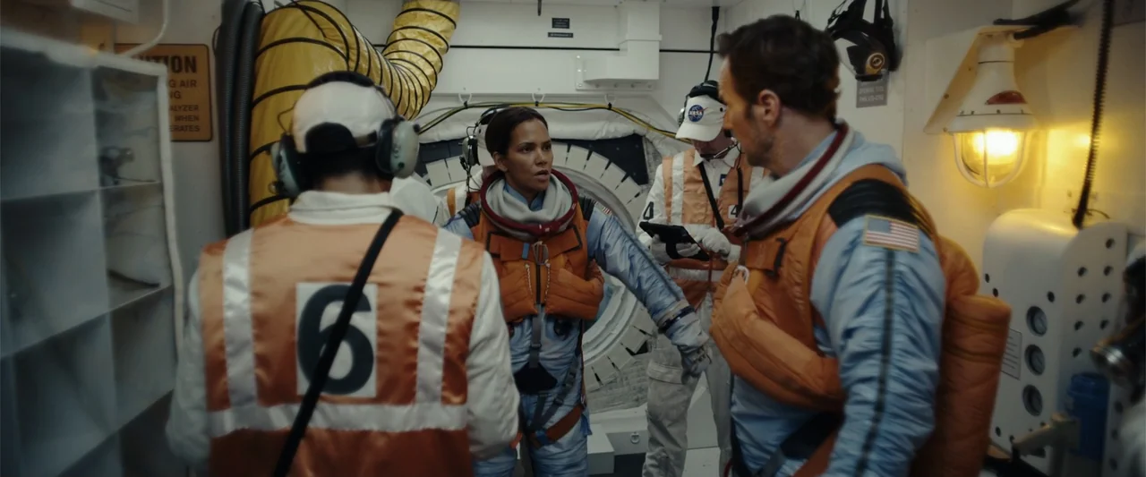 Moonfall (2022) movie still: medium — A cramped and technical spacecraft interior features rounded airlocks and white paneled bulkheads. Four people…