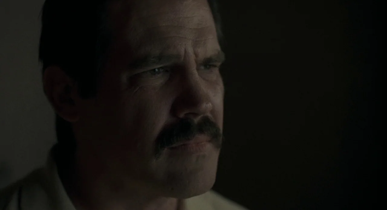 American Gangster (2007) movie still: closeup — A dimly lit room with the subject in partial shadow. A man with a thick mustache stares blankly into…
