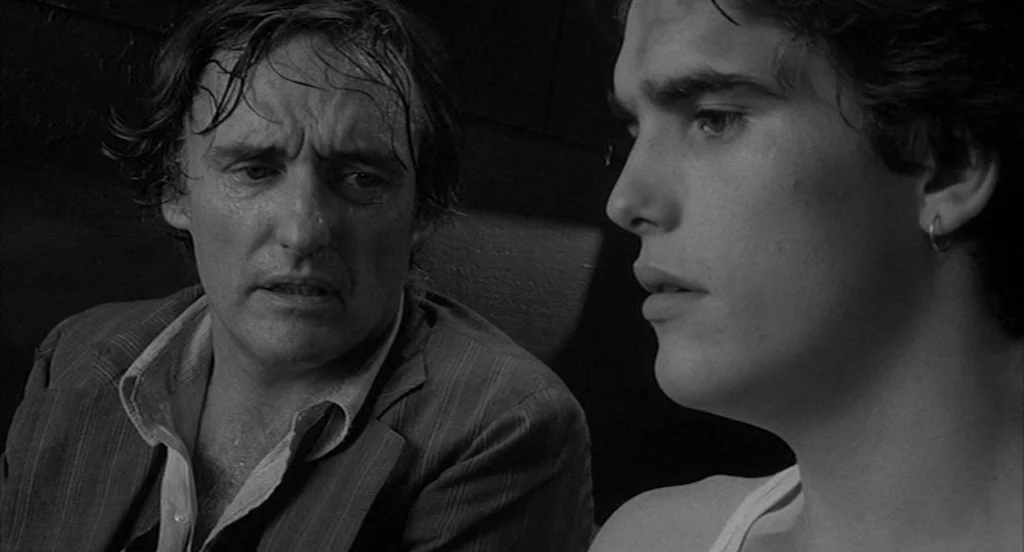Rumble Fish (1983) movie still: medium — The interior of a dark, cramped vehicle during nighttime. Two men sit side by side in close proximity.