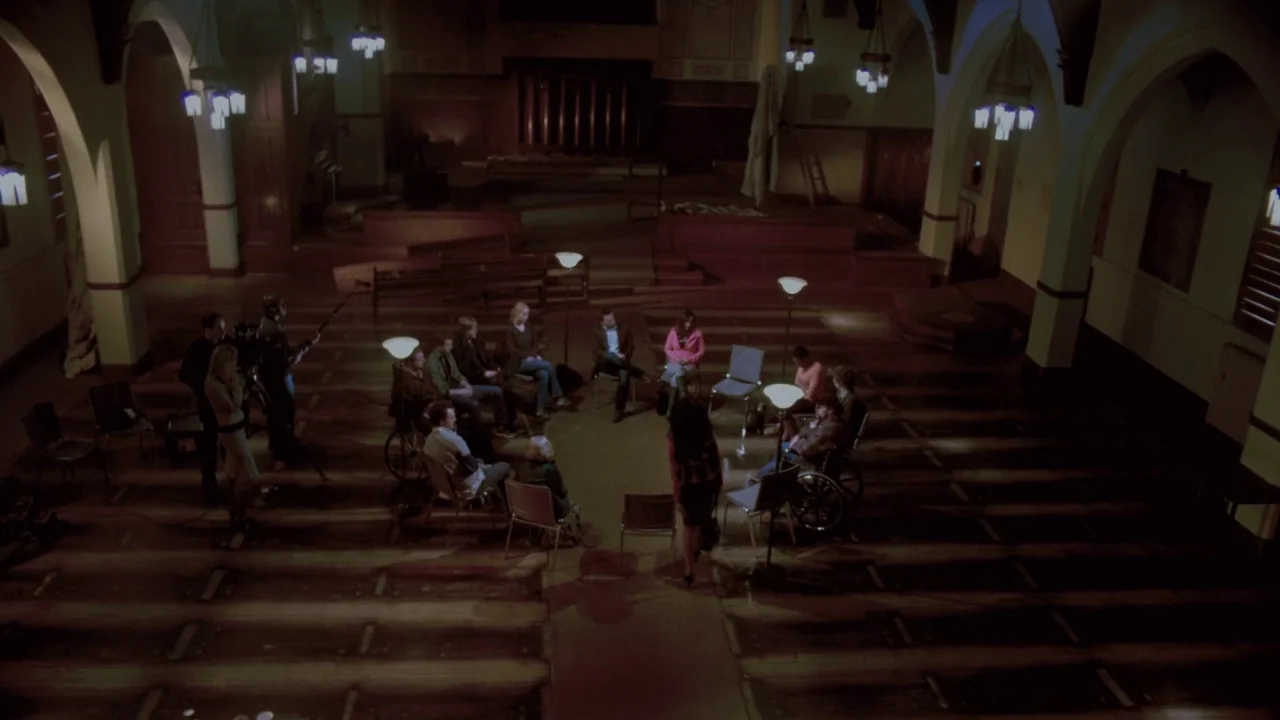 Saw VII: The Final Chapter (2010) movie still: wide — A spacious hall with arched columns and wooden flooring holds a group meeting. Several people…
