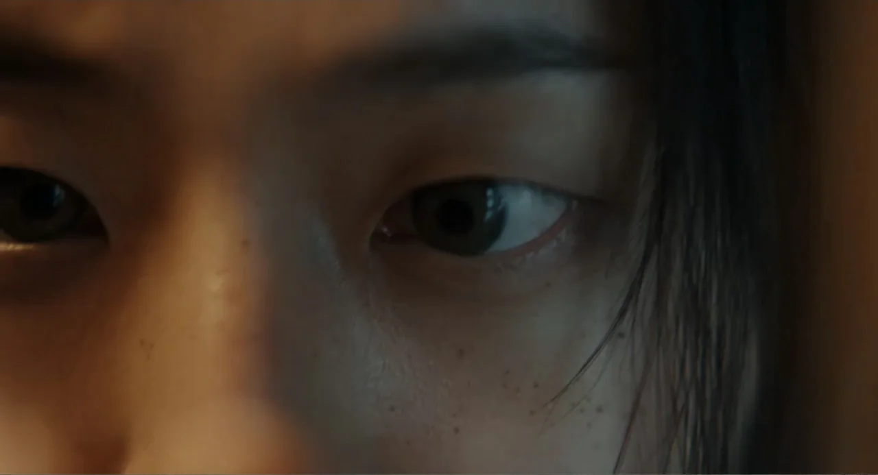 Winter in Sokcho (2025) movie still: closeup — A close view of a person's eyes and nose in a plain indoor setting. The subject looks directly toward…