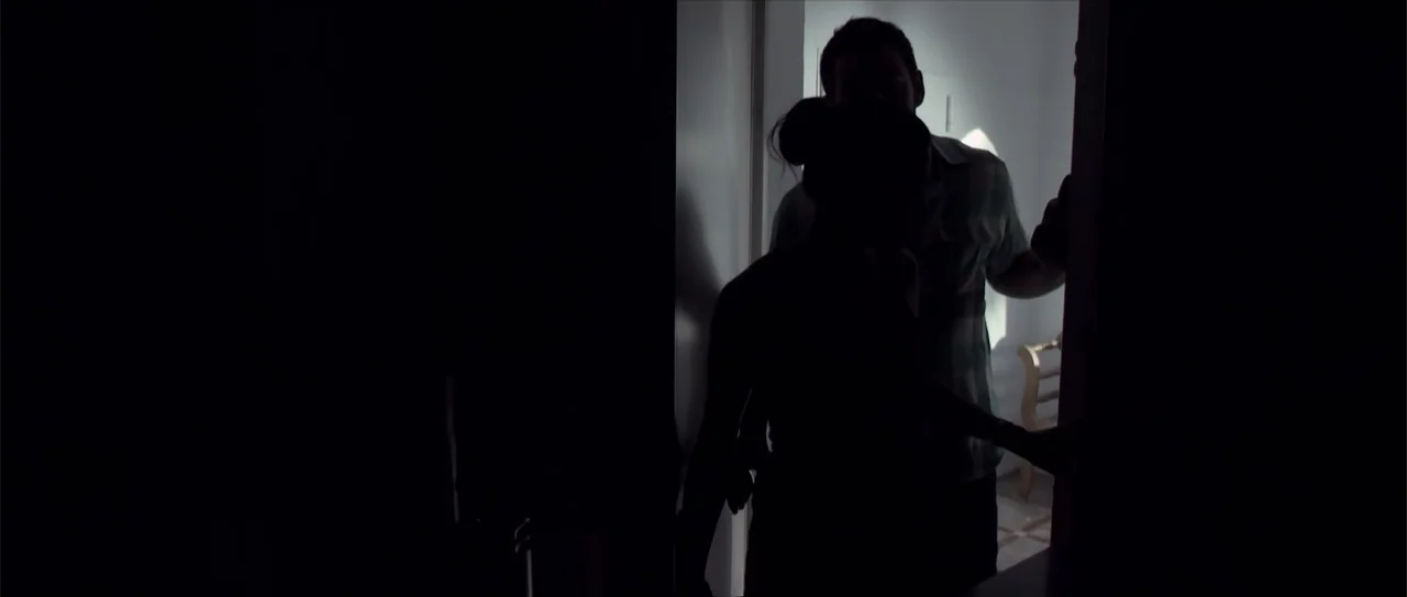 Otro verano (2013) movie still: medium — A silhouette of two figures stands in a bright doorway connecting two rooms. The woman faces the man who…