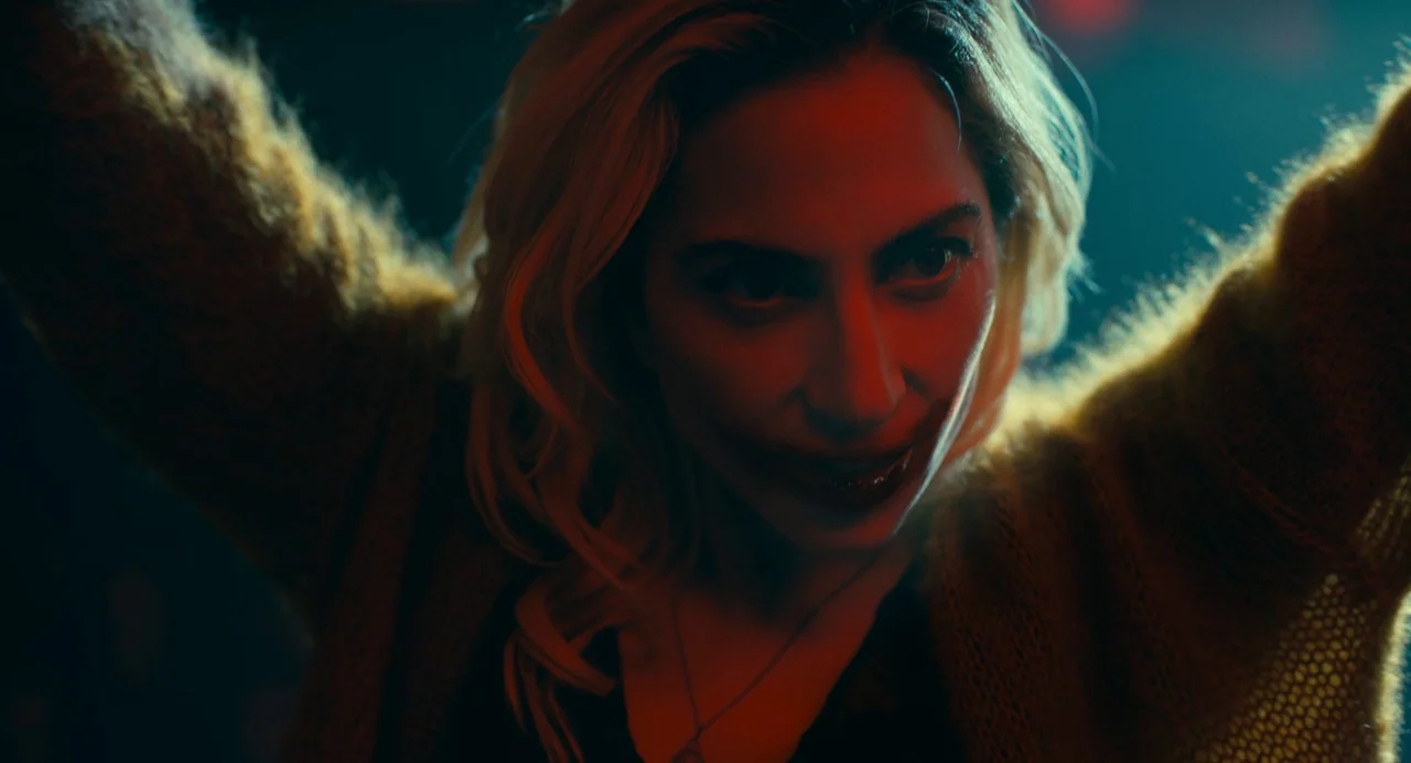 Joker: Folie à Deux (2024) movie still: closeup — A dark environment lit by saturated red and blue artificial lighting. A woman with blonde hair…