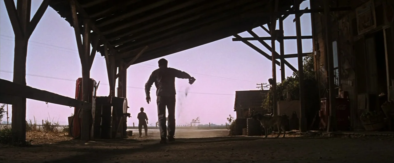 Cool Hand Luke (1967) movie still: wide — A rural gasoline station sits under a large wooden roof structure during the day. A man walks away from…