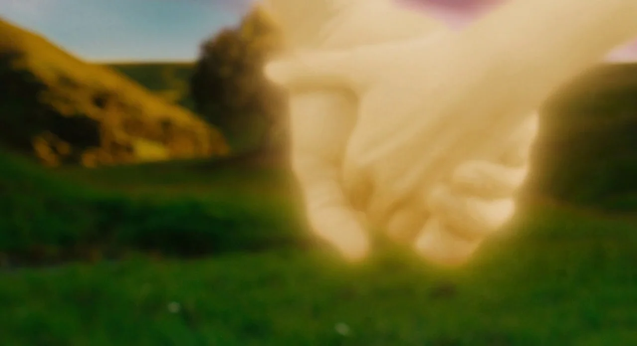Noah (2014) movie still: closeup — An open grassy field under a bright sky serves as a blurred background. Two human hands clasp together, heavily…
