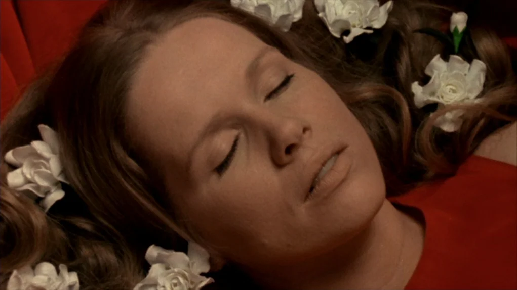 Face to Face (1976) movie still: closeup — A woman lies still on a vibrant red fabric surface decorated with white flowers. She has her eyes closed…