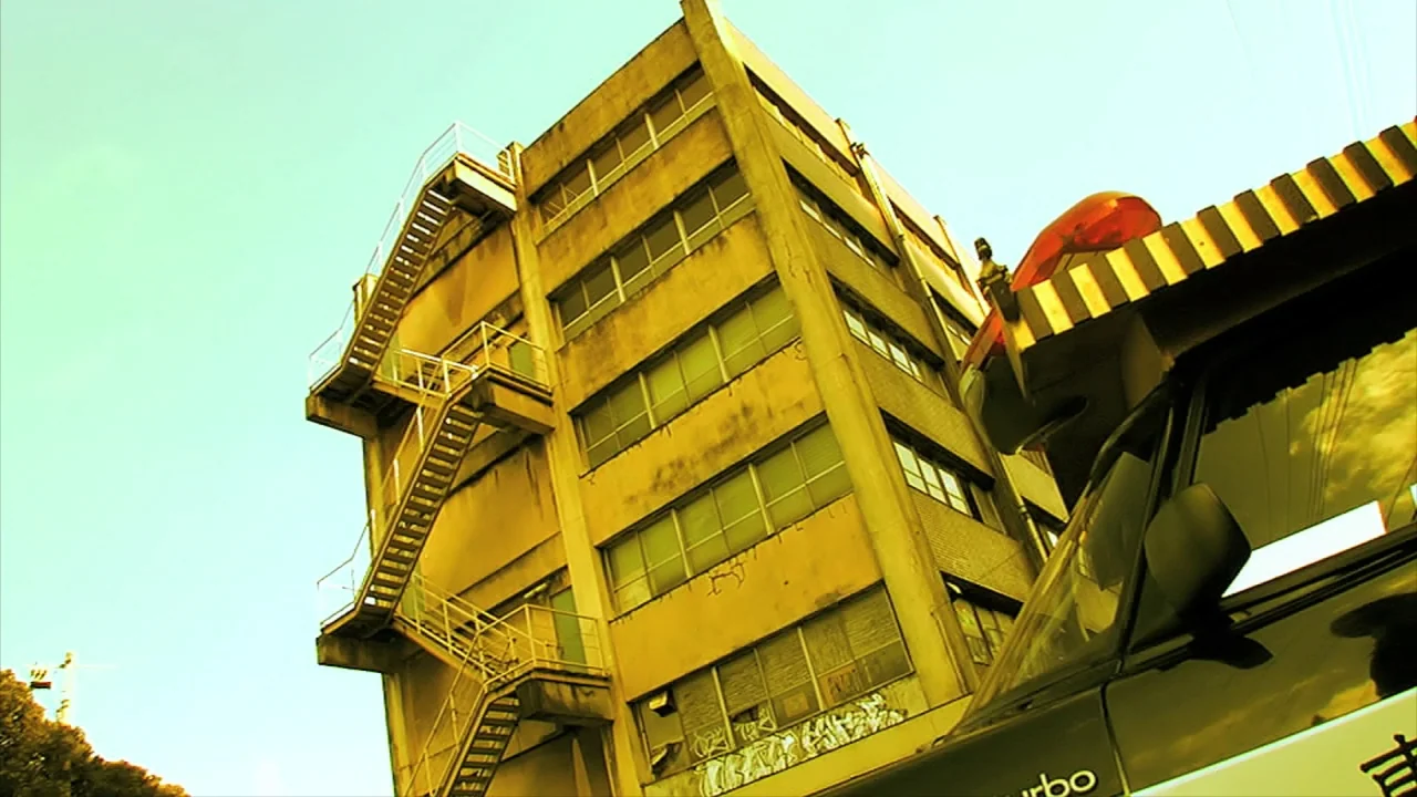 Tokyo Gore Police (2008) movie still: wide — A multi-story concrete industrial building features an external metal staircase running up its side.…