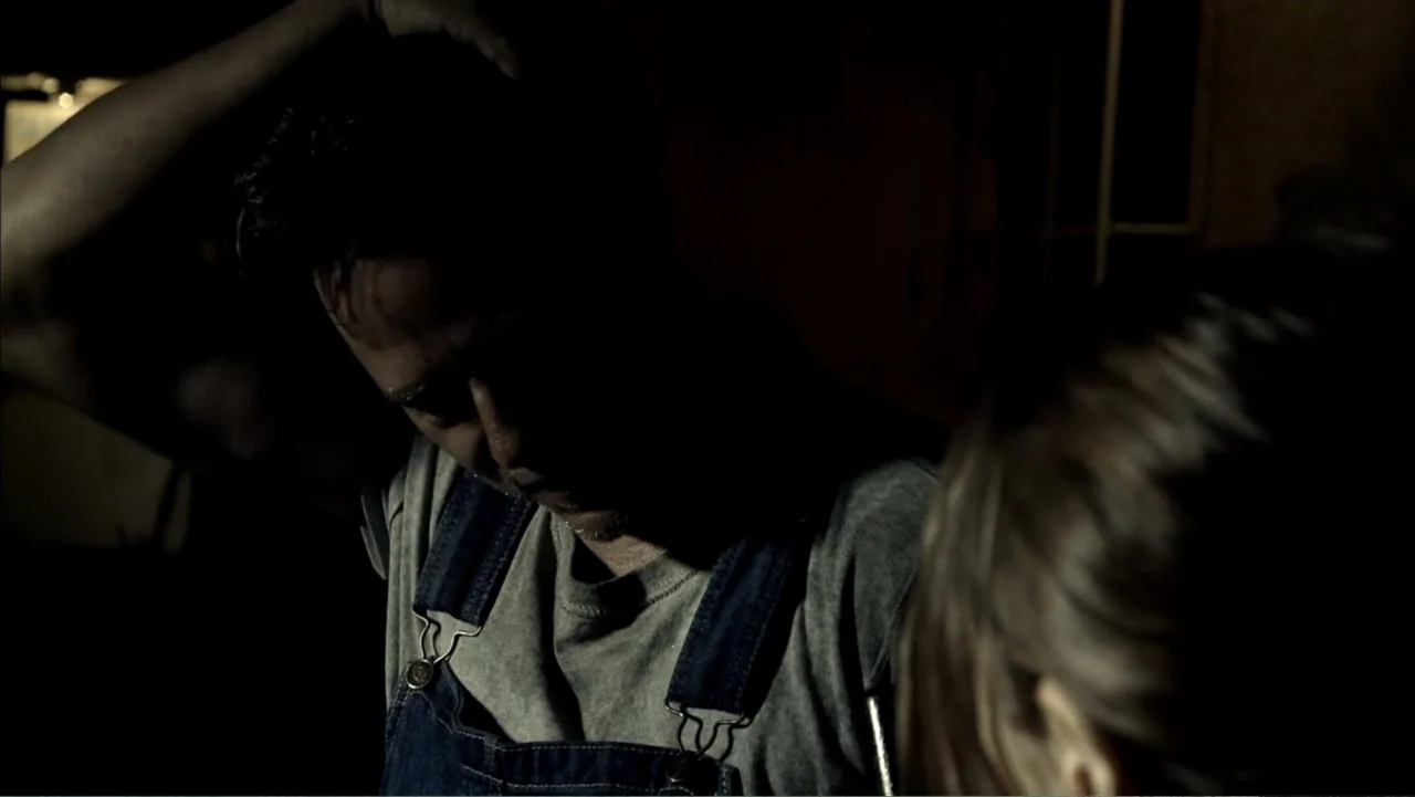 Abandoned Dead (2015) movie still: medium — A dark, dimly lit interior space with shadows obscuring most architectural details. A man in denim…