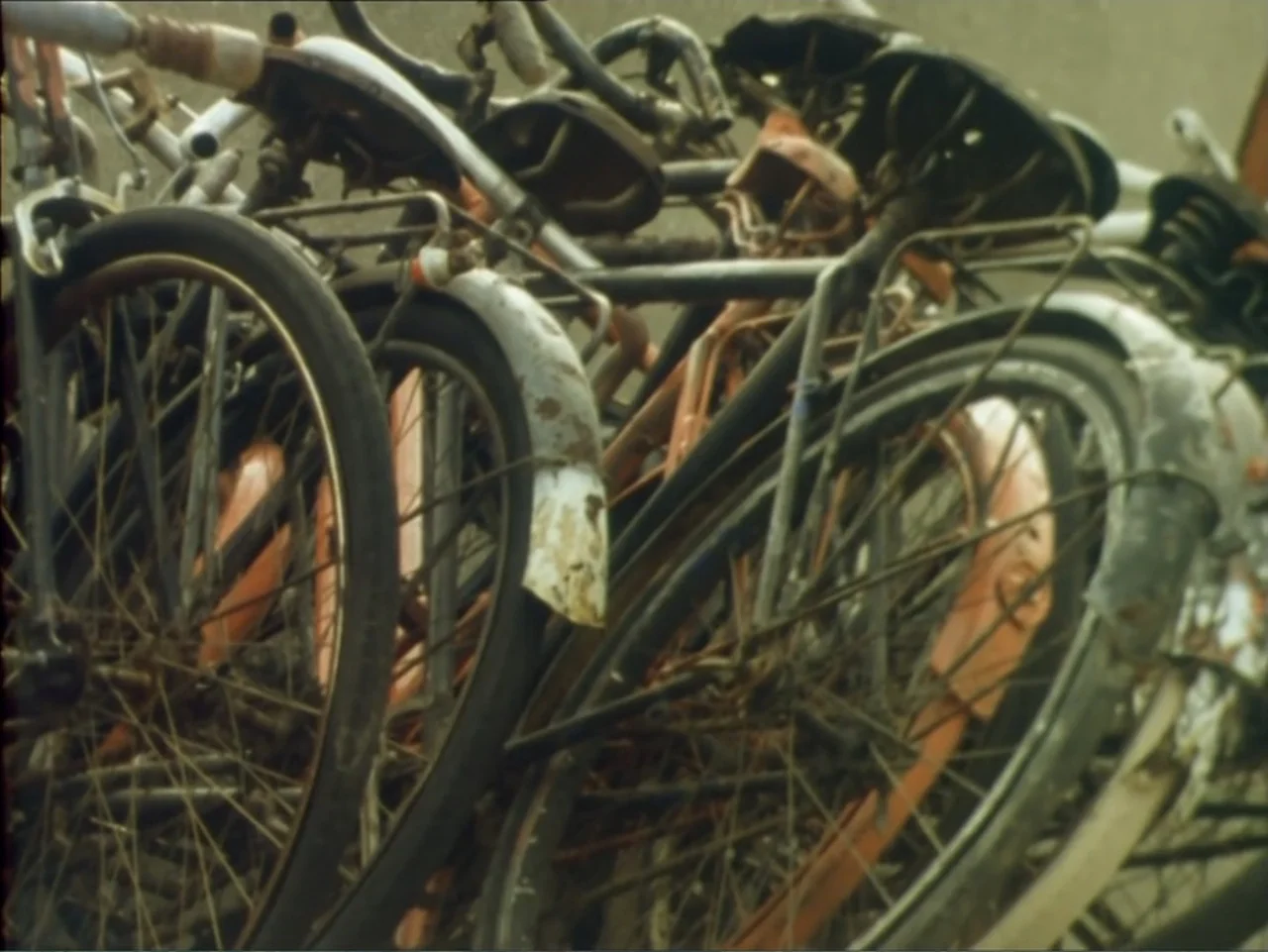 A Dessert for Constance (1981) movie still: closeup — A pile of old bicycles with weathered frames and rusted fenders is closely packed. No people…