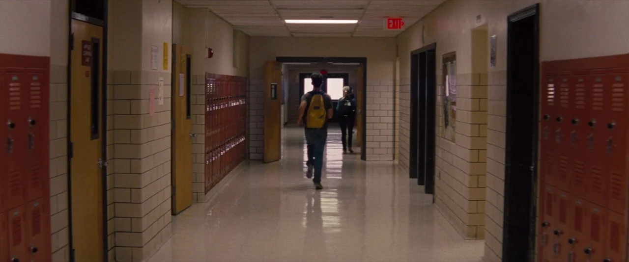 The Spectacular Now (2013) movie still: fullbody — A long school corridor features cream-colored brick walls and rows of orange metal lockers. A…