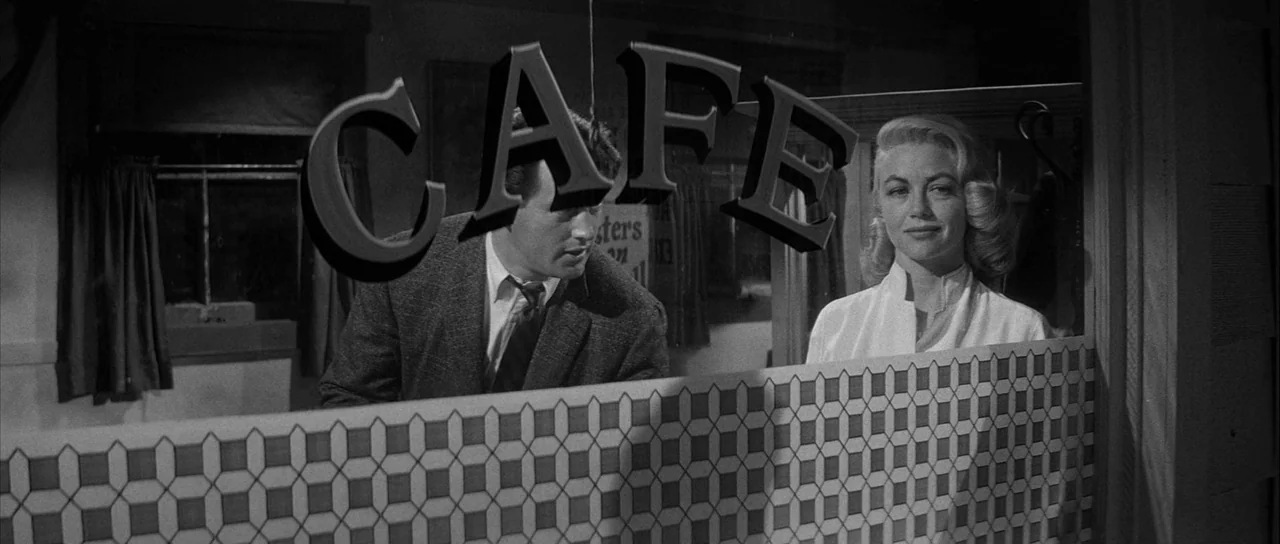 The Tarnished Angels (1957) movie still: medium — A man and a woman stand behind a partition in a diner window. The window has the word CAFE written…