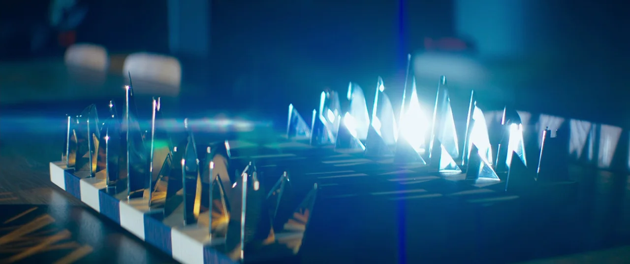 Inside (2023) (2023) movie still: closeup — A close-up view of a stylized modern chess set on a dark board. Sharp metallic pieces glint under…