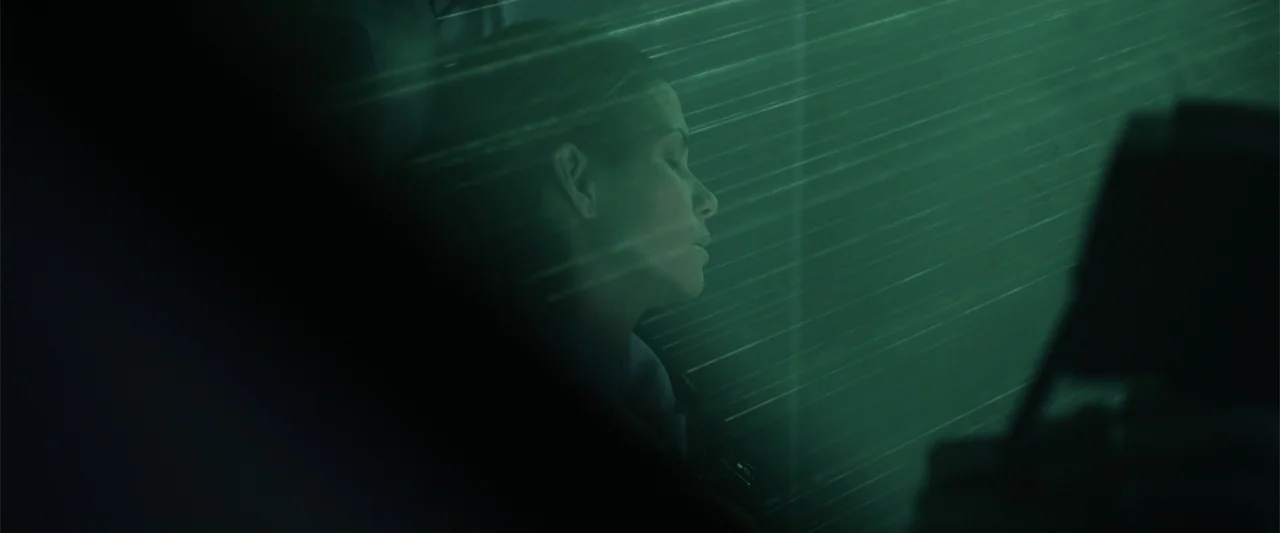 Moonfall (2022) movie still: closeup — A dark vehicle interior is filled with horizontal lines of green light. A woman with closed eyes sits still…