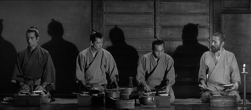 Red Beard (1965) movie still: wide — A dark wooden room with sliding panels features four men kneeling in a line. They are eating from individual…