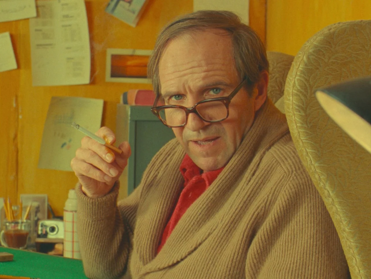 The Rat Catcher (2023) movie still: medium — A workspace features yellow walls adorned with various papers and a small photograph. An older man sits…