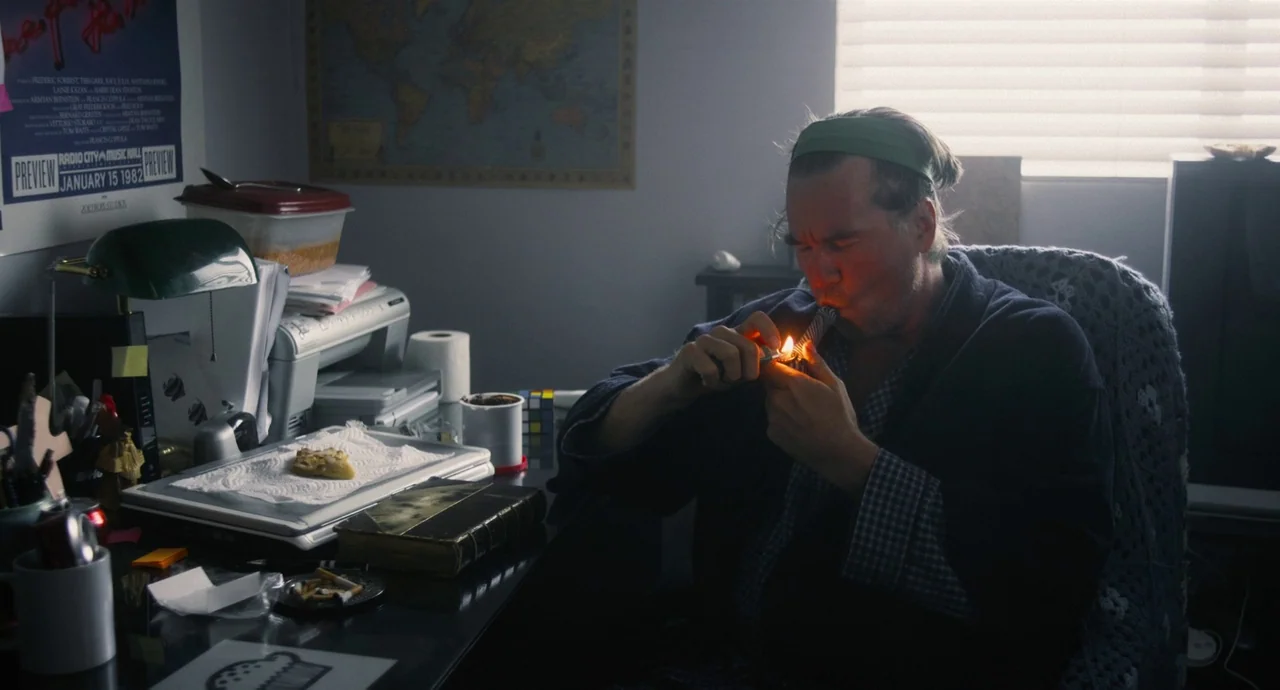 Palo Alto (2013) movie still: medium — A cluttered desk workspace sits in front of a man wearing a green headband. The man sits in a cushioned chair…