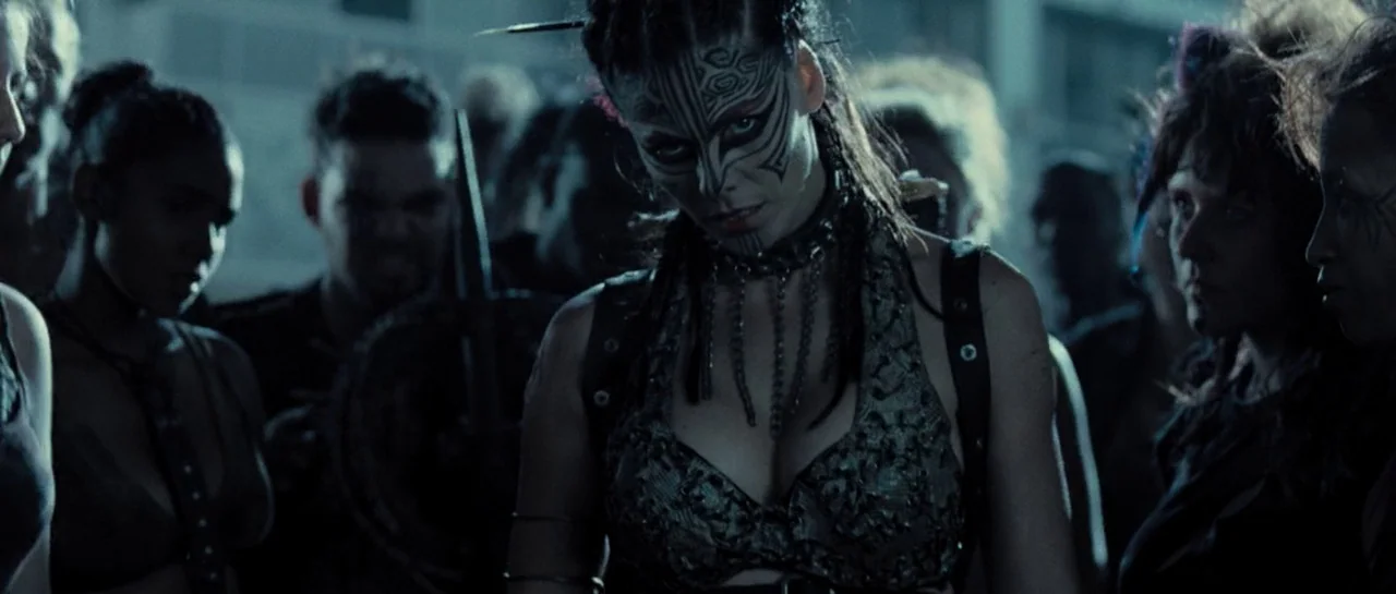 Doomsday (2008) movie still: medium — An interior industrial space filled with people surrounding a central female figure. The central woman wears…