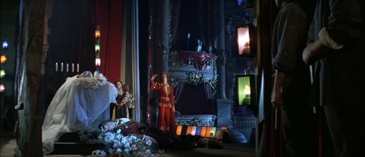Ludwig (1973) movie still: wide — A dark theater interior features a central dais covered in white fabric and flowers. A costumed actor stands near…