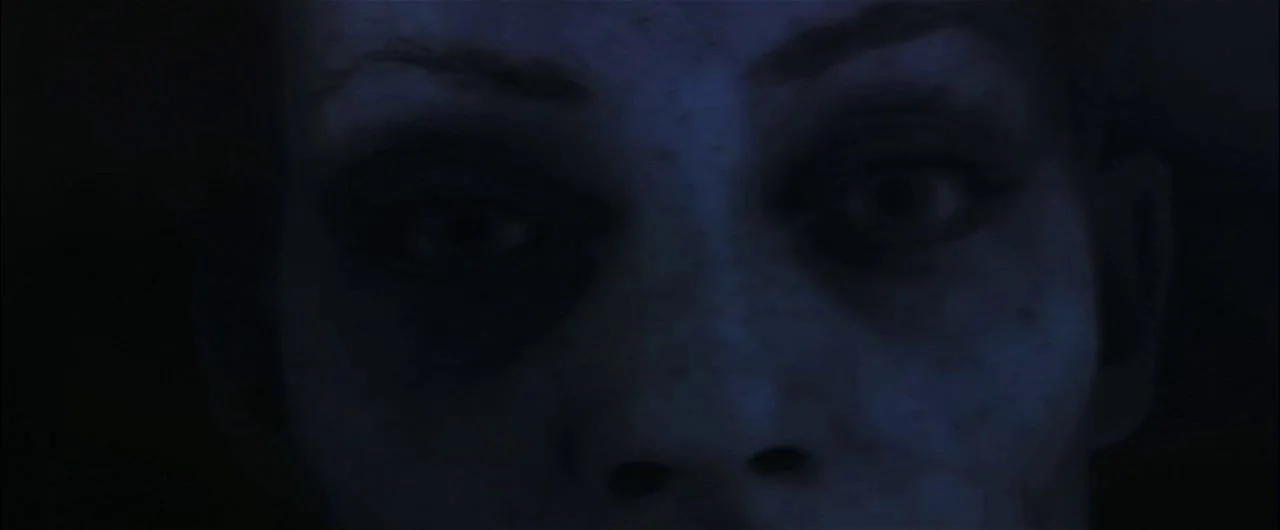 What Lies Beneath (2000) movie still: closeup — A dark, underexposed interior space is occupied only by a face in shadows. A person stares directly…
