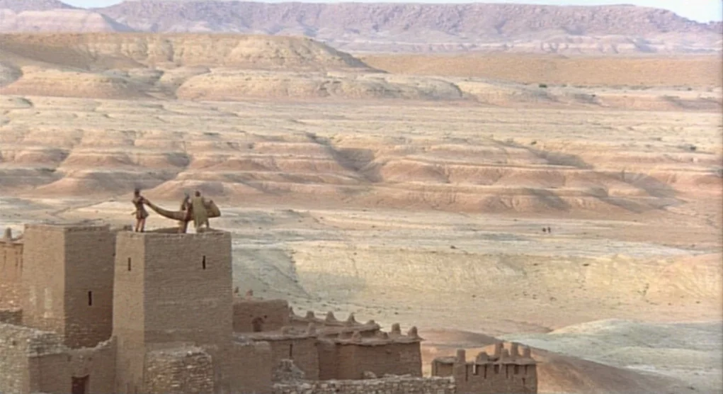 Time Bandits (1981) movie still: wide — A vast, arid desert landscape features rolling sand dunes under an expansive sky. Two figures stand on the…