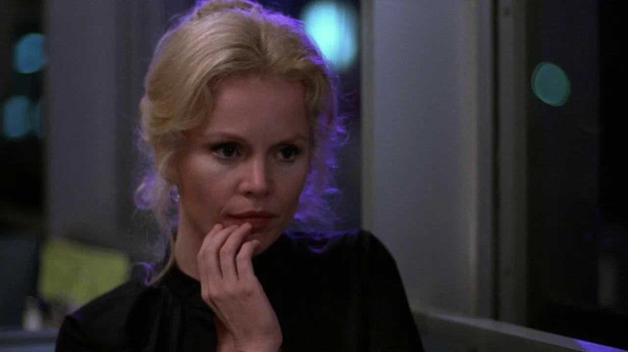 Thief (1981) movie still: closeup — The interior of a commuter train car is dark with out-of-focus city lights visible. A blonde woman sits near a…